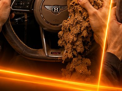 Hands pulling sculpted clay away from a Bentley steering wheel