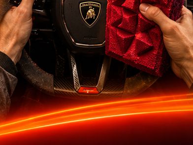 A hand pressing dense red foam against a Lamborghini steering wheel